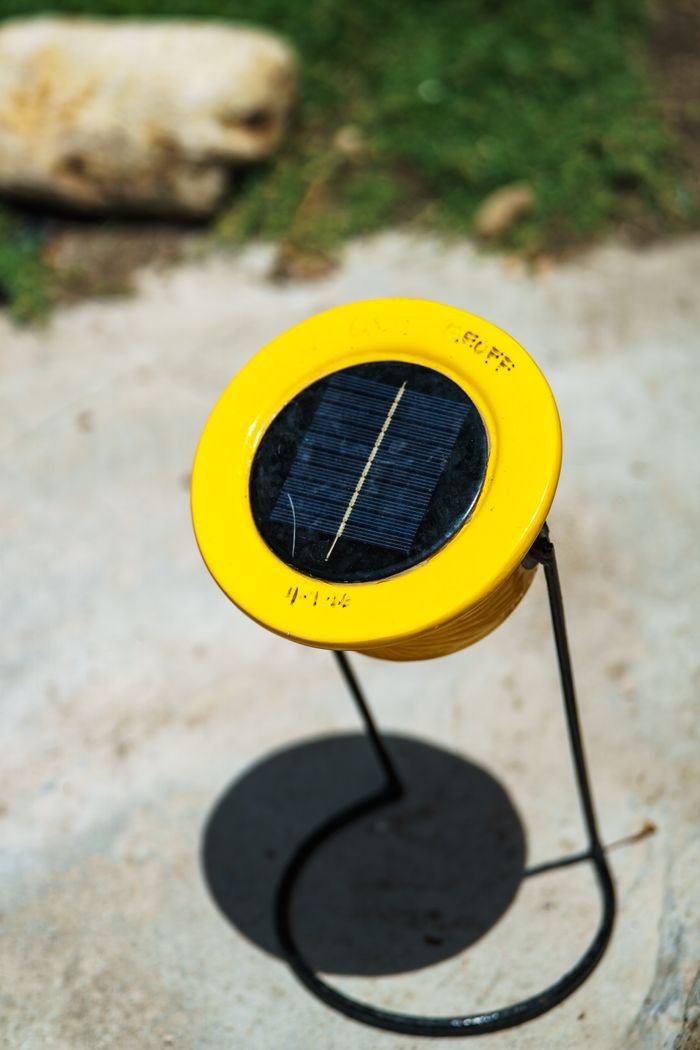 A yellow solar-powered garden light stands outdoors on a sunny day, casting a shadow.