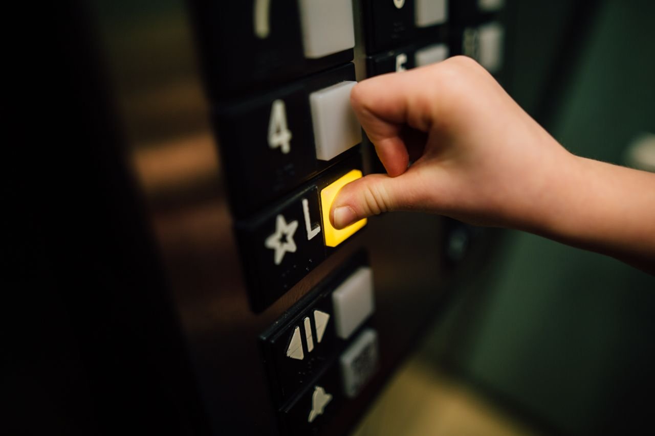 High angle of crop unrecognizable person pressing button of modern elevator with thumb